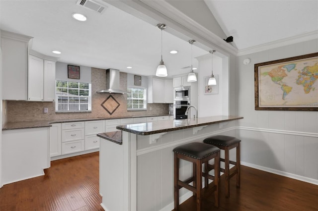 kitchen featuring visible vents, wall chimney range hood, dark wood finished floors, dark stone countertops, and appliances with stainless steel finishes