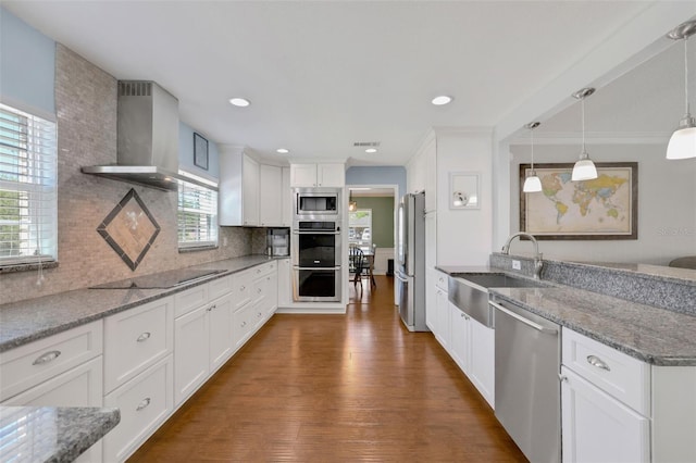 kitchen with backsplash, appliances with stainless steel finishes, a peninsula, wall chimney exhaust hood, and a sink