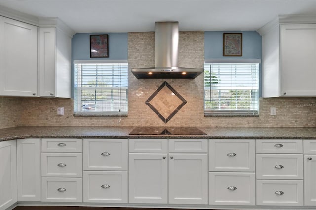 kitchen featuring black electric cooktop, dark countertops, white cabinets, and wall chimney range hood