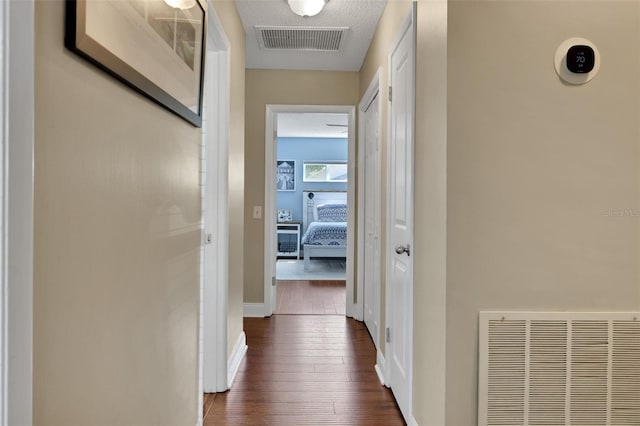 corridor featuring baseboards, dark wood-style floors, visible vents, and a textured ceiling