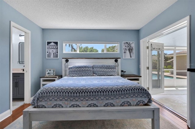 bedroom featuring ensuite bath, access to exterior, wood finished floors, and a textured ceiling