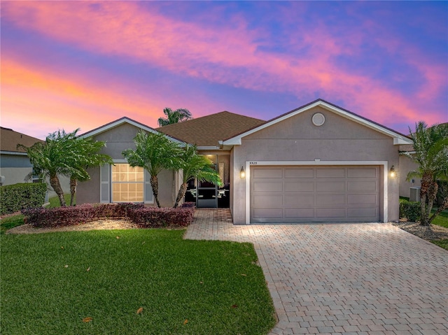ranch-style home with decorative driveway, stucco siding, and a yard