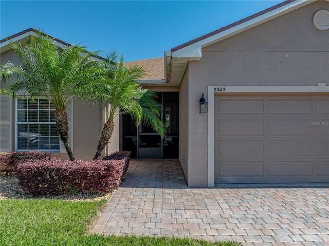 entrance to property featuring stucco siding, a garage, and roof with shingles