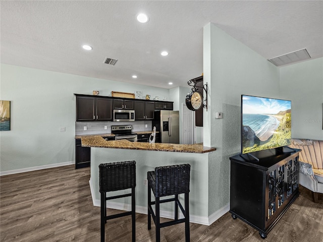 kitchen featuring a breakfast bar, baseboards, dark wood finished floors, appliances with stainless steel finishes, and backsplash