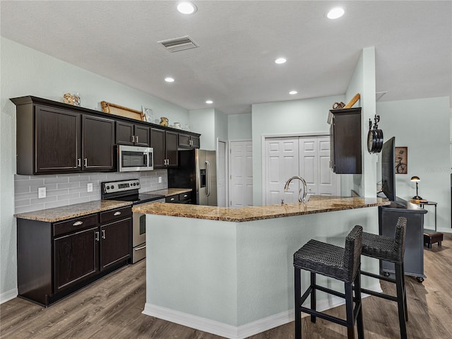 kitchen with tasteful backsplash, light stone counters, wood finished floors, and stainless steel appliances