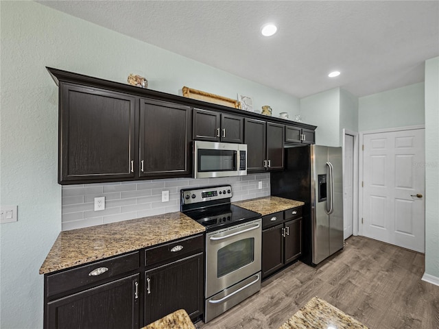 kitchen featuring light wood finished floors, recessed lighting, tasteful backsplash, appliances with stainless steel finishes, and light stone counters