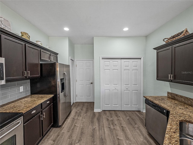 kitchen with dark brown cabinetry, tasteful backsplash, wood finished floors, stainless steel appliances, and dark stone counters