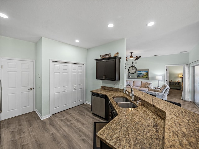 kitchen featuring dark wood-style flooring, dark stone countertops, a sink, dishwasher, and a peninsula