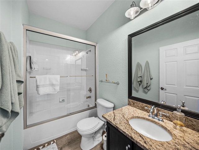 full bath featuring vanity, toilet, a textured wall, bath / shower combo with glass door, and wood finished floors