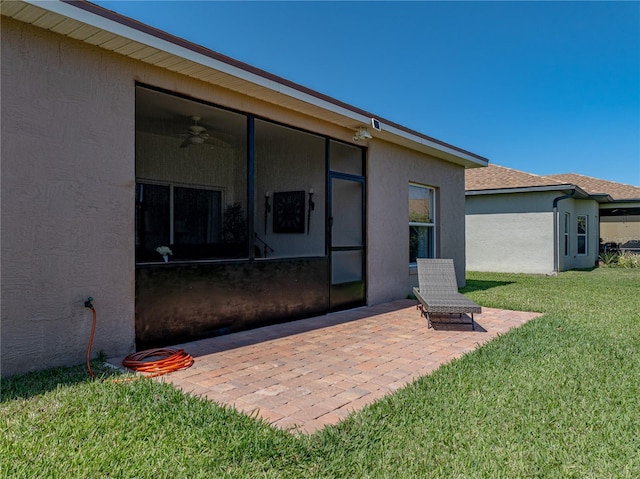 rear view of house featuring a lawn, stucco siding, a sunroom, and a patio area