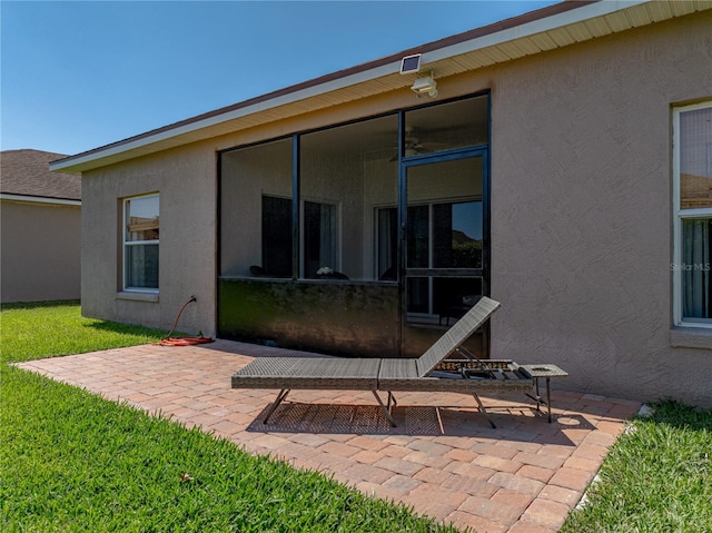 rear view of property with a lawn, a sunroom, stucco siding, and a patio area