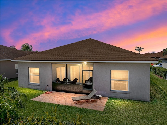 back of property with a shingled roof, a lawn, stucco siding, and a patio area