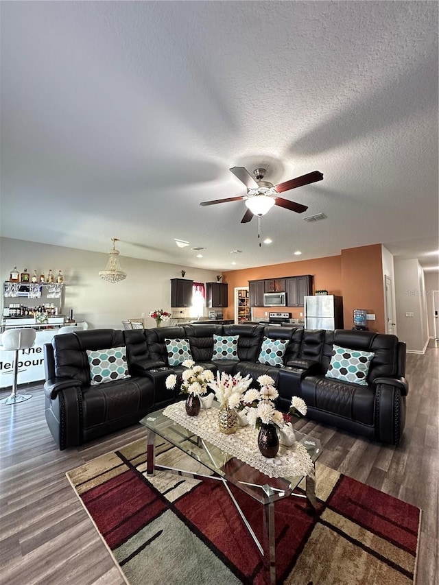 living room with wood finished floors, a ceiling fan, visible vents, and a textured ceiling