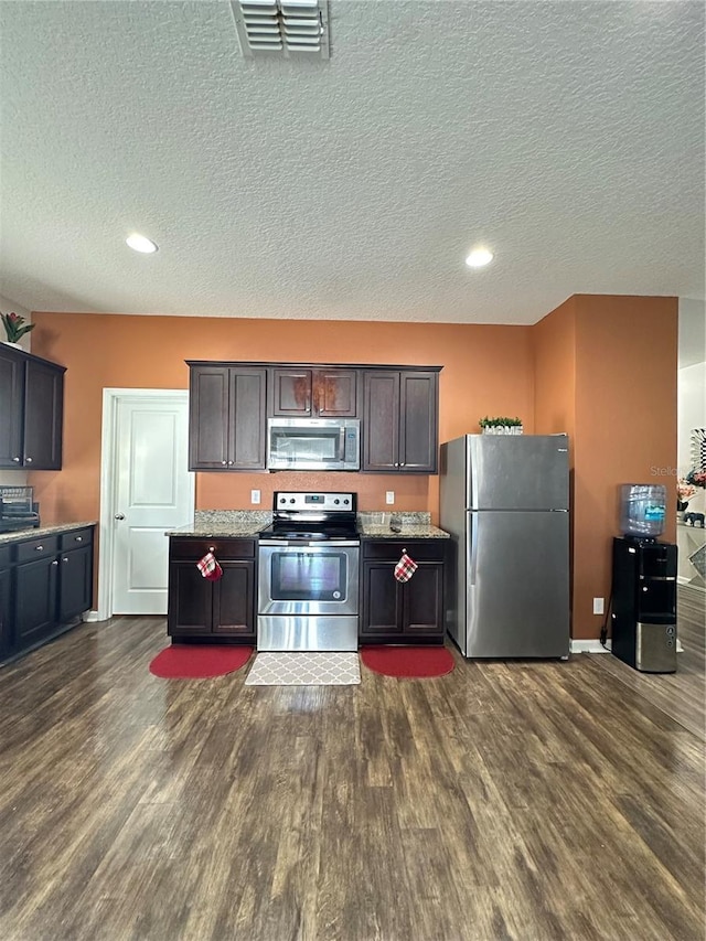 kitchen featuring visible vents, dark wood-type flooring, light stone counters, appliances with stainless steel finishes, and a textured ceiling