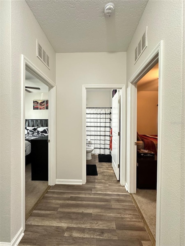 corridor featuring visible vents, baseboards, a textured ceiling, and dark wood-style flooring