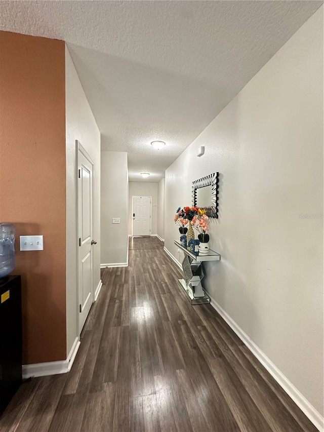 hallway with baseboards, dark wood-type flooring, and a textured ceiling