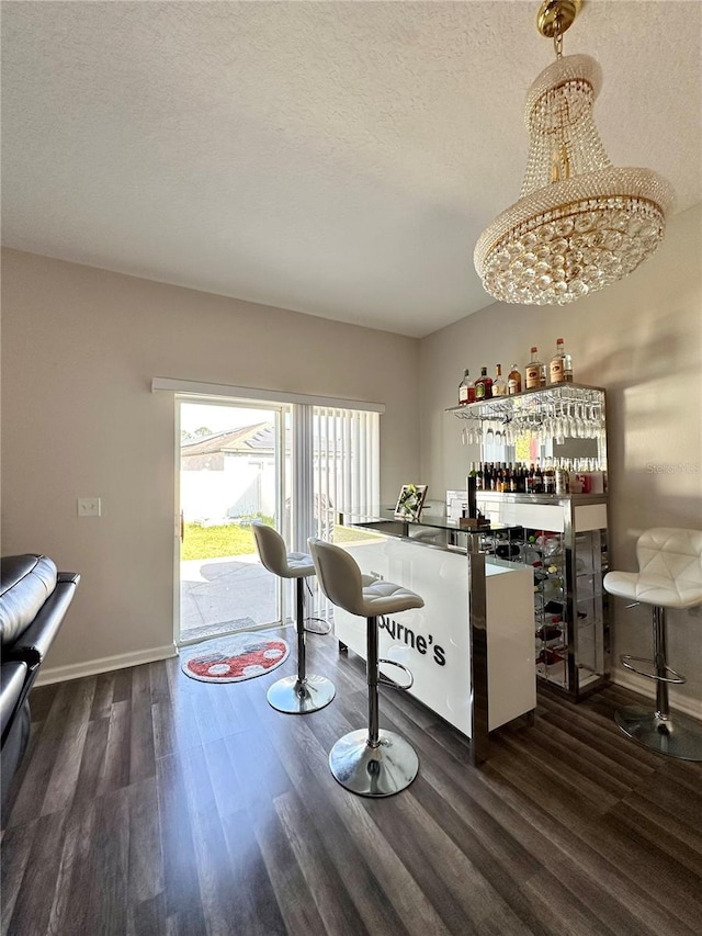 bar with a bar, baseboards, dark wood-style flooring, and a textured ceiling