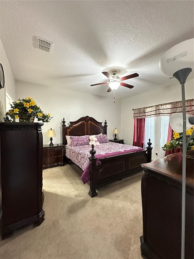 bedroom with a textured ceiling, a ceiling fan, visible vents, and light carpet