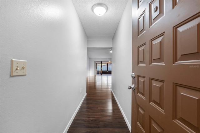 hall with baseboards, a textured ceiling, and dark wood-style flooring