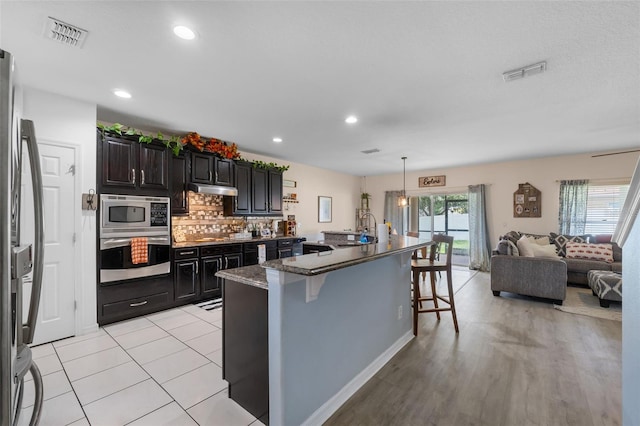 kitchen with visible vents, under cabinet range hood, appliances with stainless steel finishes, a breakfast bar area, and decorative backsplash