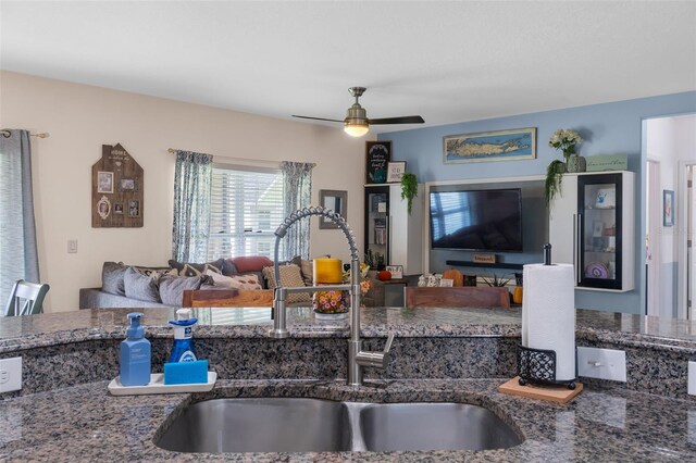 kitchen with open floor plan, dark stone counters, a ceiling fan, and a sink
