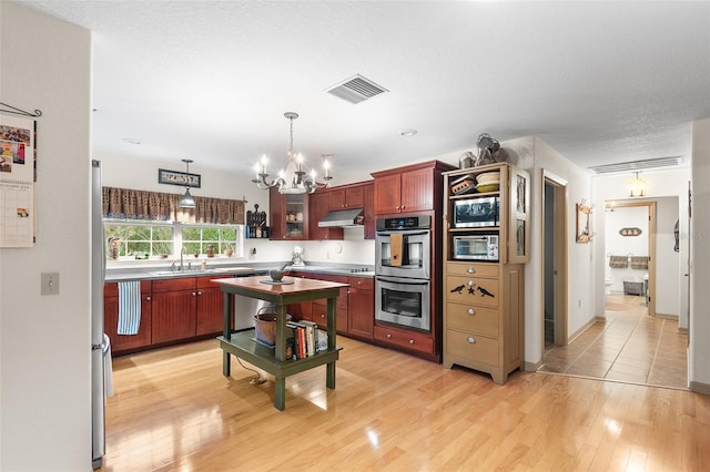 5020 Broadmore Dr, Auburndale, FL 33823 - kitchen featuring under cabinet range hood, appliances with stainless steel finishes, a chandelier, light wood-type flooring, and reddish brown cabinets