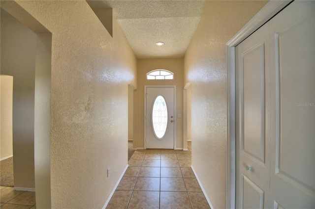 doorway to outside featuring light tile patterned flooring, a textured wall, baseboards, and a textured ceiling