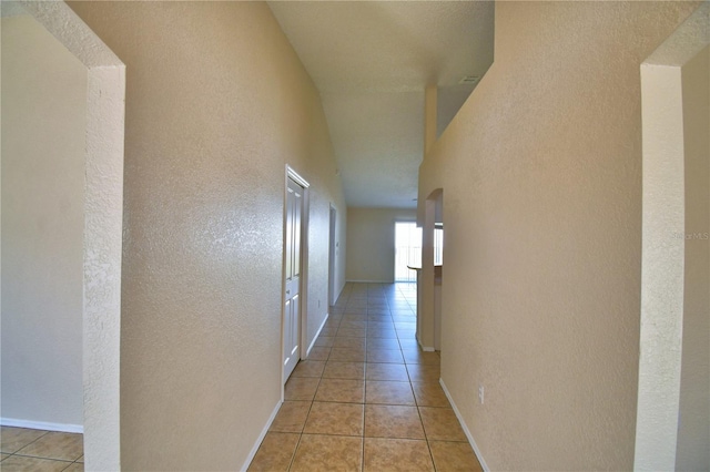 corridor with baseboards, a textured wall, and light tile patterned floors