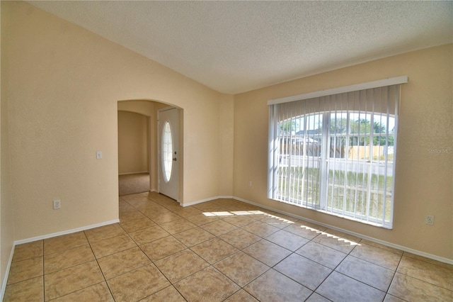 empty room with light tile patterned flooring, lofted ceiling, arched walkways, and a textured ceiling