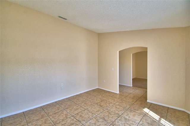 unfurnished room with a textured ceiling, light tile patterned floors, baseboards, visible vents, and arched walkways