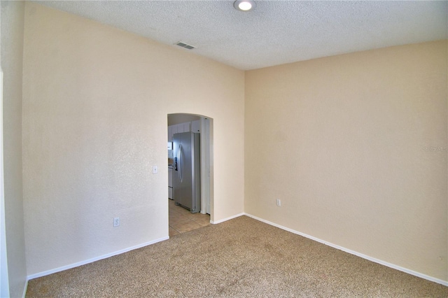 unfurnished room featuring a textured ceiling, visible vents, baseboards, arched walkways, and light colored carpet