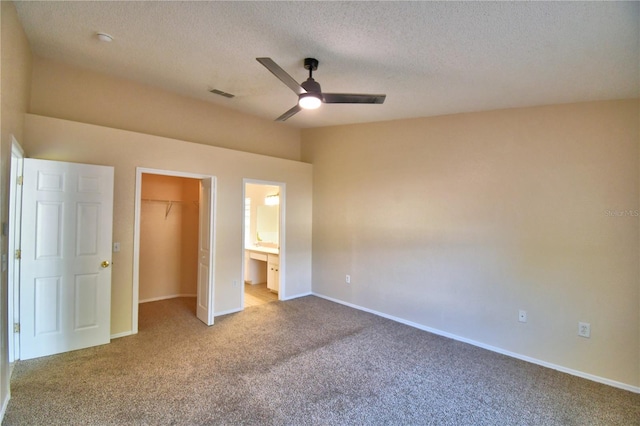 unfurnished bedroom featuring a closet, carpet floors, a walk in closet, baseboards, and visible vents