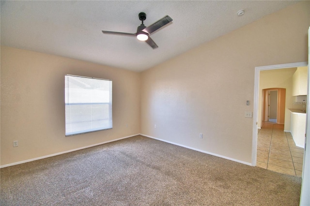 spare room featuring vaulted ceiling, a ceiling fan, baseboards, light tile patterned floors, and light colored carpet