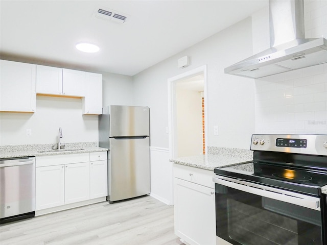 1801 3rd Ct SE, Winter Haven, FL 33880 - kitchen with stainless steel appliances, wall chimney exhaust hood, a sink, light wood-type flooring, and white cabinetry