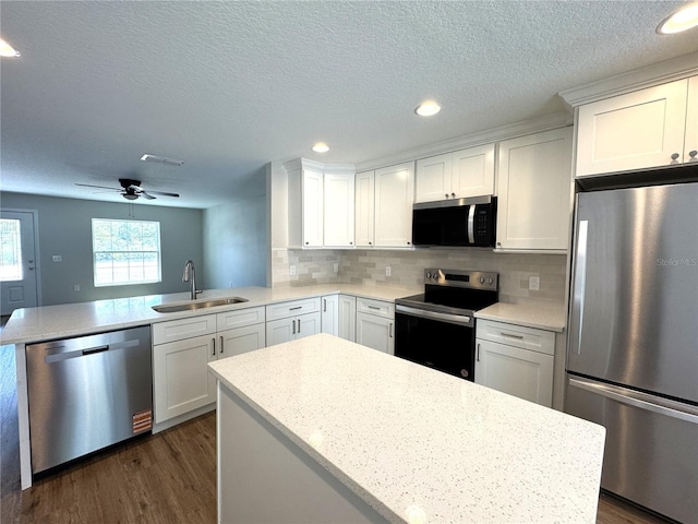 kitchen featuring white cabinetry, a sink, dark wood-style floors, a peninsula, and appliances with stainless steel finishes