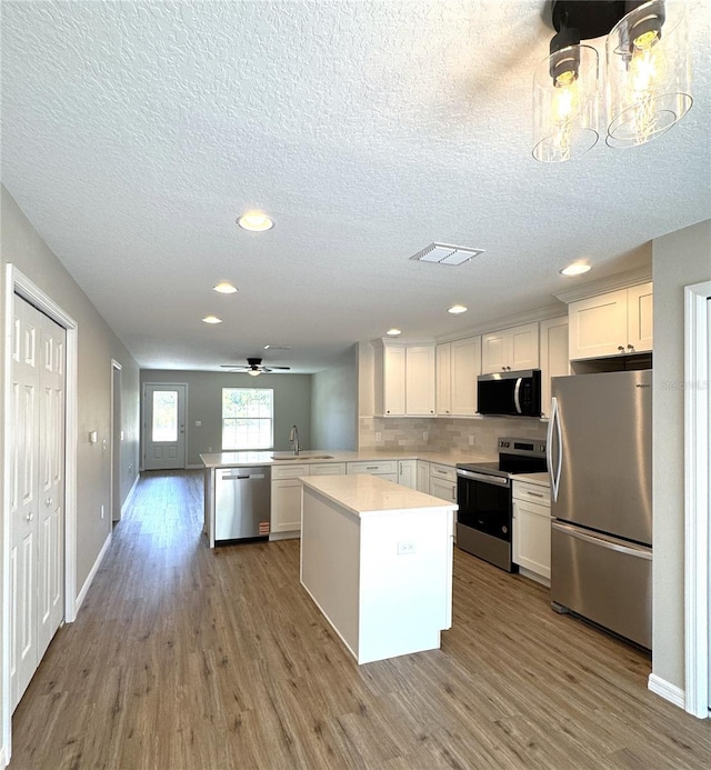 kitchen featuring light countertops, a peninsula, appliances with stainless steel finishes, and wood finished floors