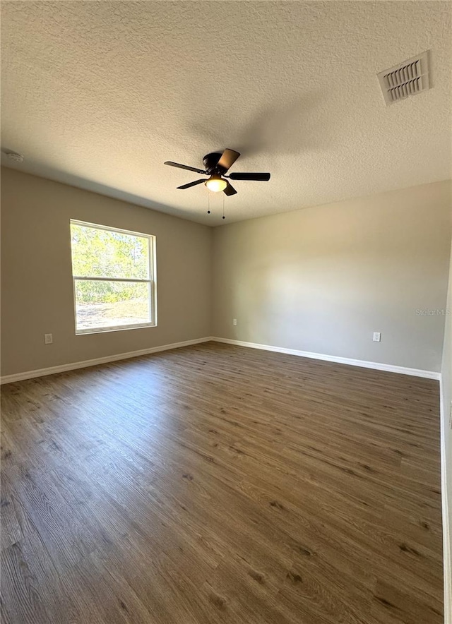 spare room featuring baseboards, dark wood-style floors, visible vents, and a ceiling fan