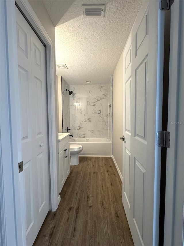 bathroom with toilet, bathing tub / shower combination, wood finished floors, a textured ceiling, and visible vents