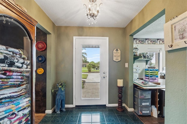 tiled foyer featuring baseboards, a textured ceiling, and an inviting chandelier