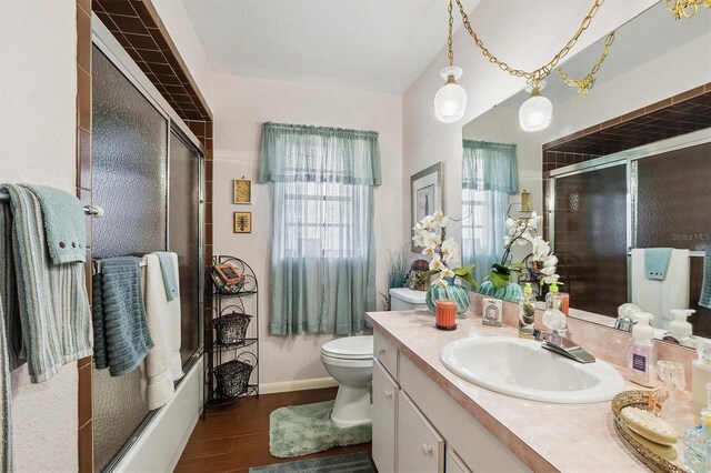 bathroom featuring vanity, toilet, baseboards, a shower with shower door, and wood finished floors