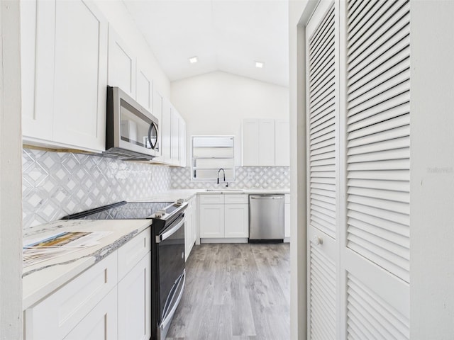kitchen with tasteful backsplash, appliances with stainless steel finishes, lofted ceiling, white cabinetry, and a sink