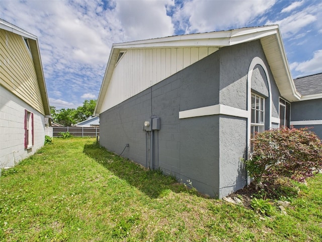 view of side of property with a lawn, fence, and concrete block siding