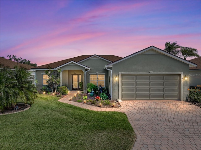 single story home with decorative driveway, stucco siding, a garage, and a lawn