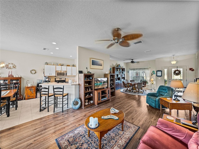 living area featuring a textured ceiling, light wood-style flooring, ceiling fan, and visible vents