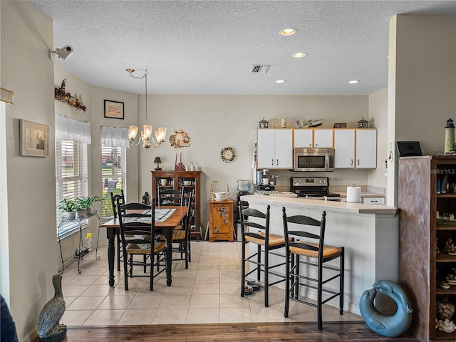 kitchen with white cabinets, visible vents, appliances with stainless steel finishes, a breakfast bar area, and a notable chandelier