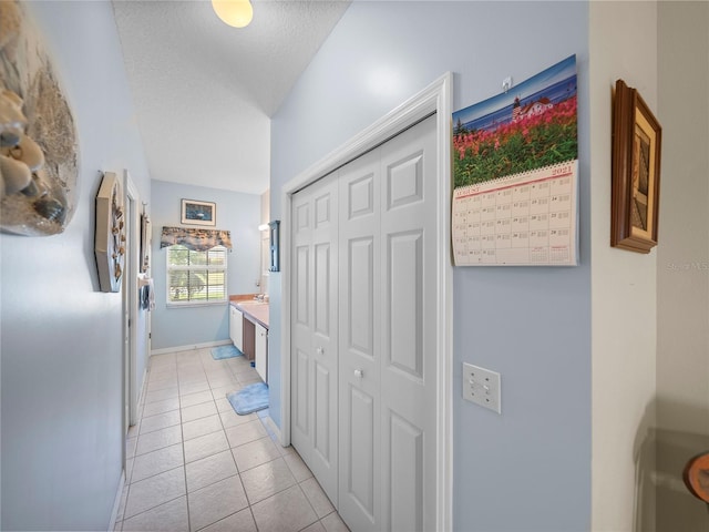 hall featuring light tile patterned flooring, baseboards, a sink, and a textured ceiling