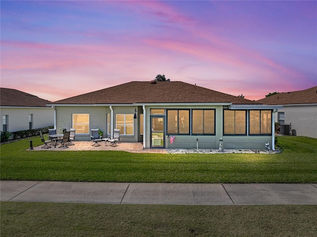rear view of property featuring a lawn, cooling unit, a patio area, and roof with shingles