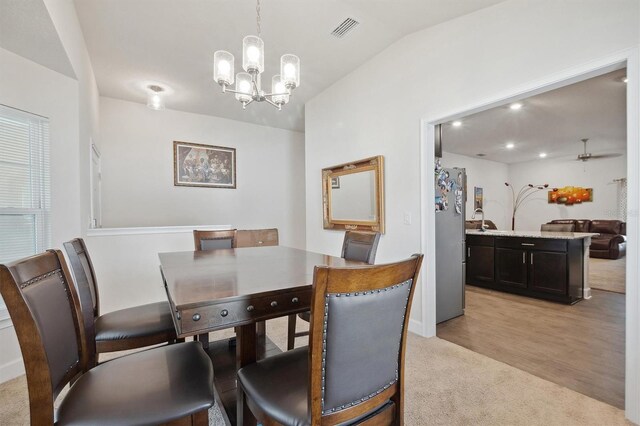 dining room with light wood-style flooring, visible vents, an inviting chandelier, vaulted ceiling, and light colored carpet