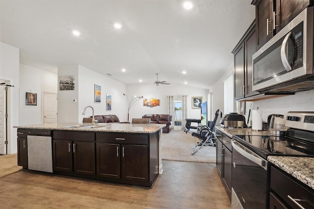 kitchen featuring open floor plan, vaulted ceiling, stainless steel appliances, a sink, and an island with sink