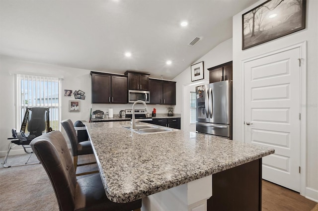 kitchen featuring stainless steel appliances, a breakfast bar, a sink, visible vents, and dark brown cabinetry